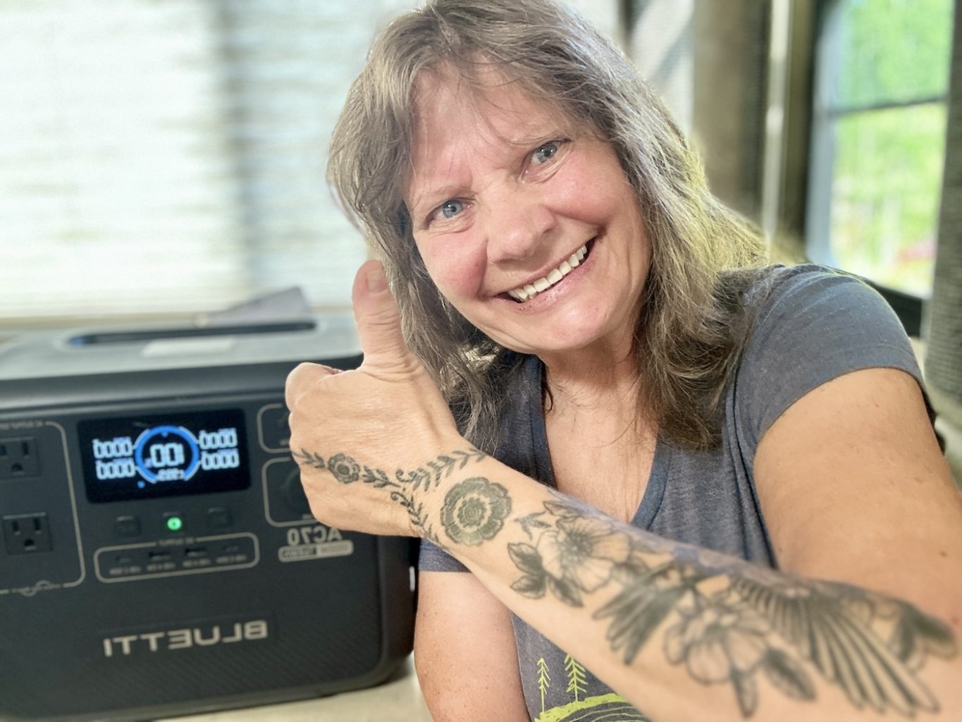 A smiling person gives a thumbs-up next to a Bluetti AC70 Portable Power Station, showcasing its digital display.