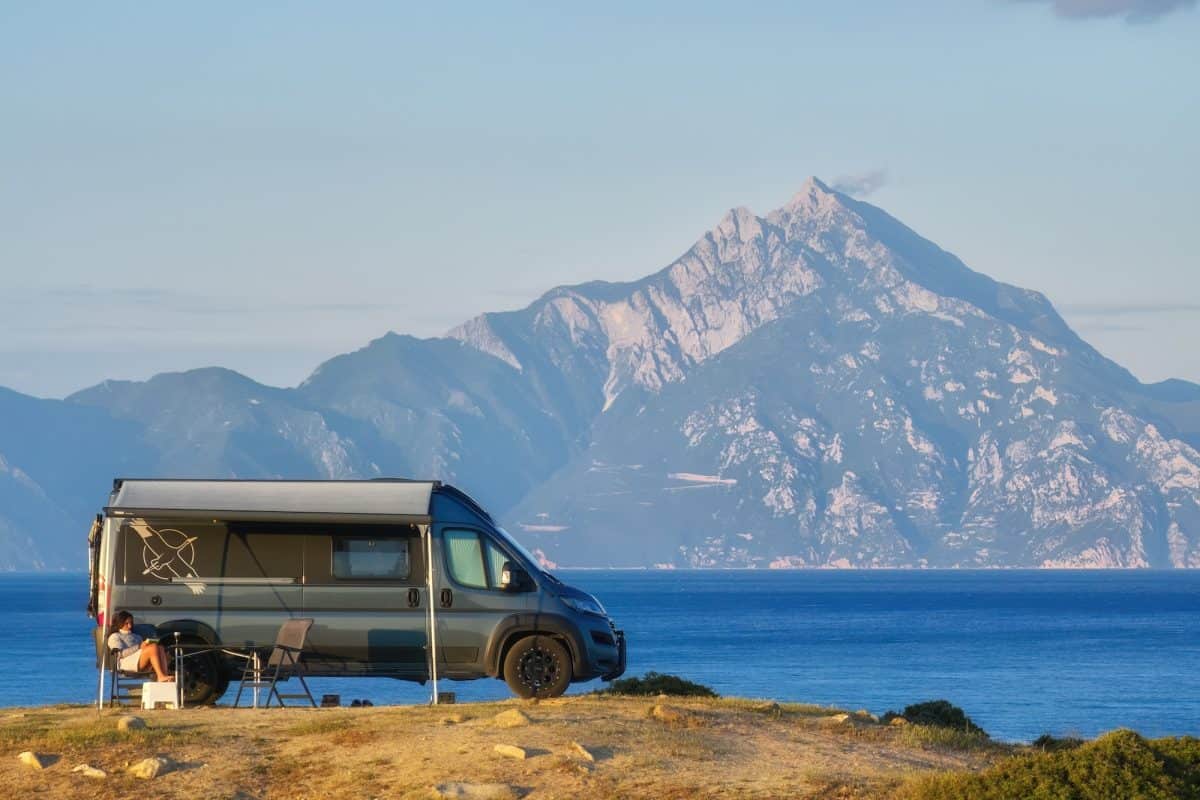 Class B RV camper van camping by lake with mountains in background